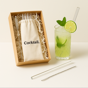 Coffret en carton kraft ouvert contenant un pochon en coton marqué « Cocktail. » avec 4 pailles en verre et une brosse de nettoyage sur papier frisotté, accompagné d’un verre de Mojito avec paille en verre et d’une paille posée à côté.
